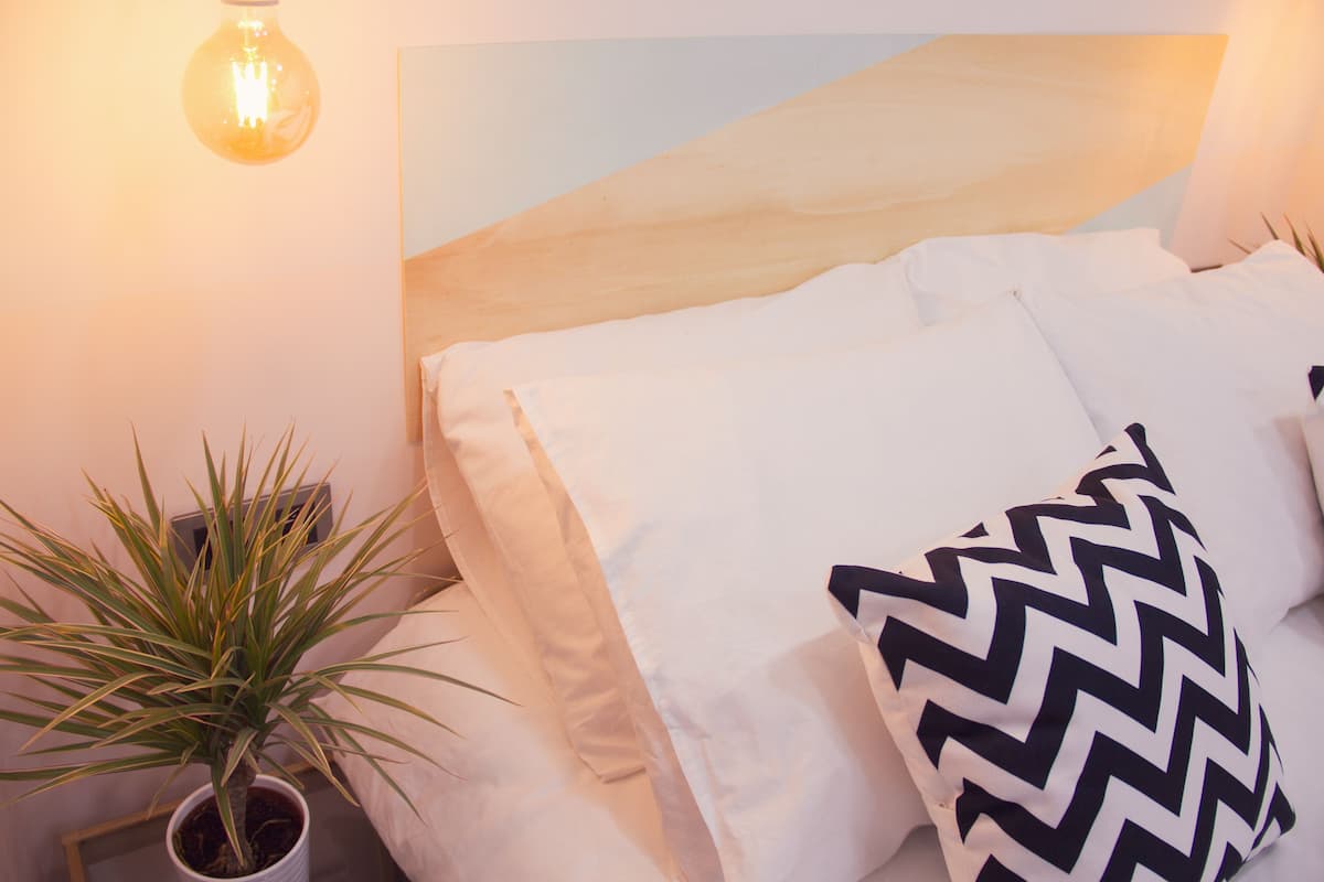 A neatly arranged bedroom with a bed, pillows, a potted plant, and a wall-mounted light fixture.