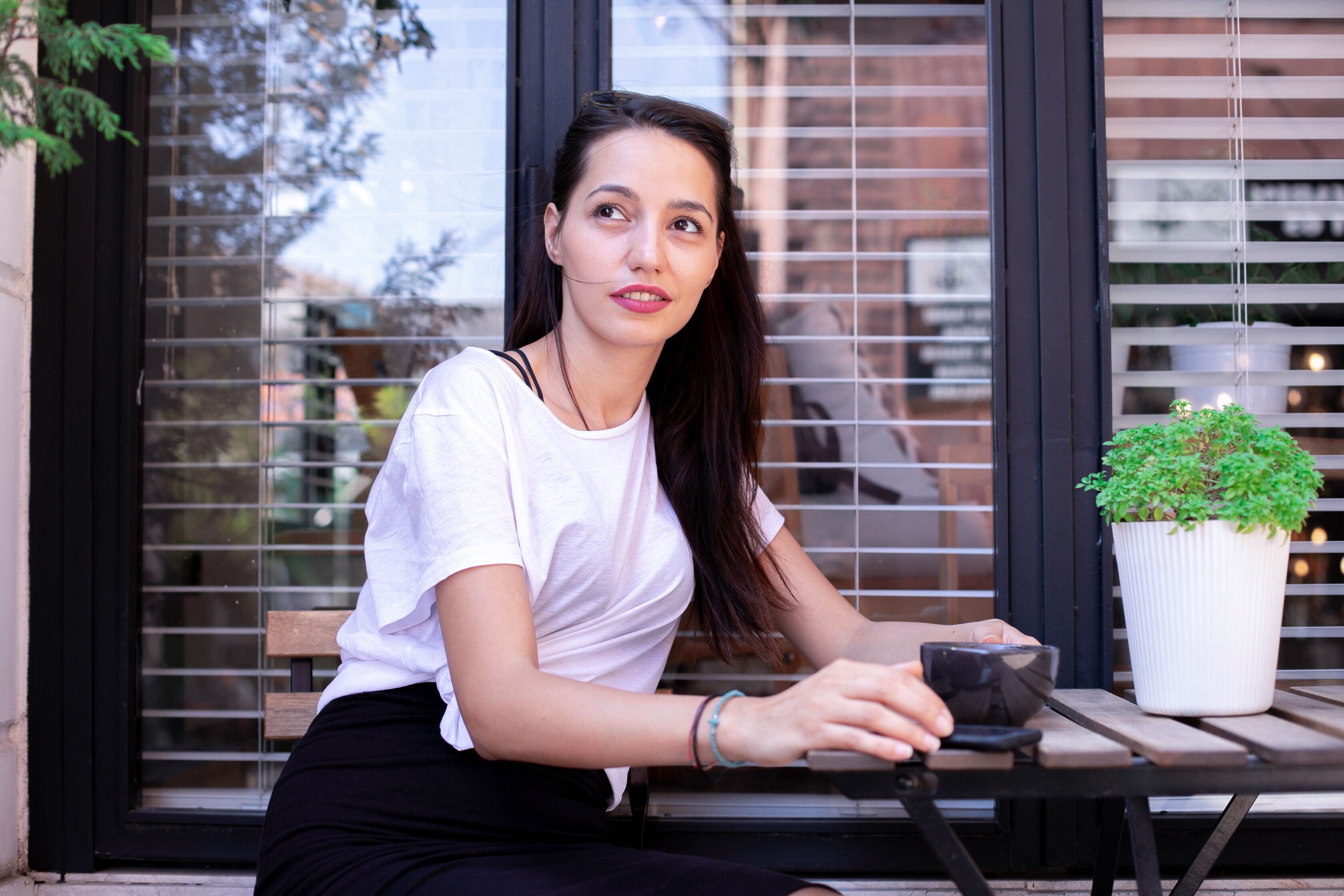 A person sitting at a table with a potted plant and a cup.