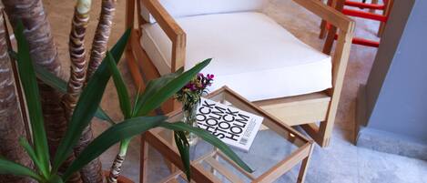 Una silla de madera con un cojín blanco, una mesita con una revista y una planta en maceta con hojas verdes.