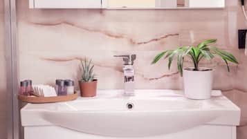 A bathroom with a white sink, a marble backsplash, a potted plant, and toiletries on a tray.