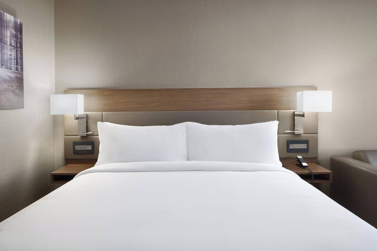 A neatly made bed with white linens, a wooden headboard, and two bedside tables with lamps and a phone.