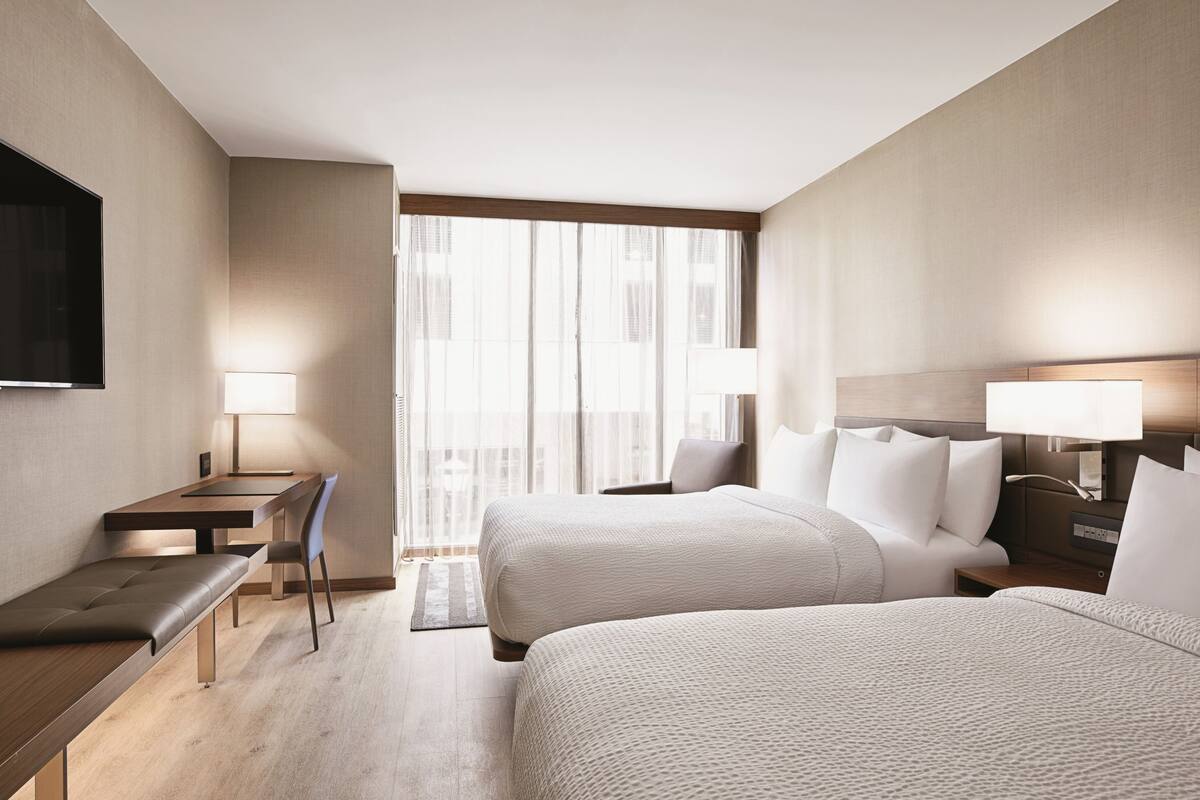 A hotel room with two beds, a desk, a chair, a TV, and a window with curtains.