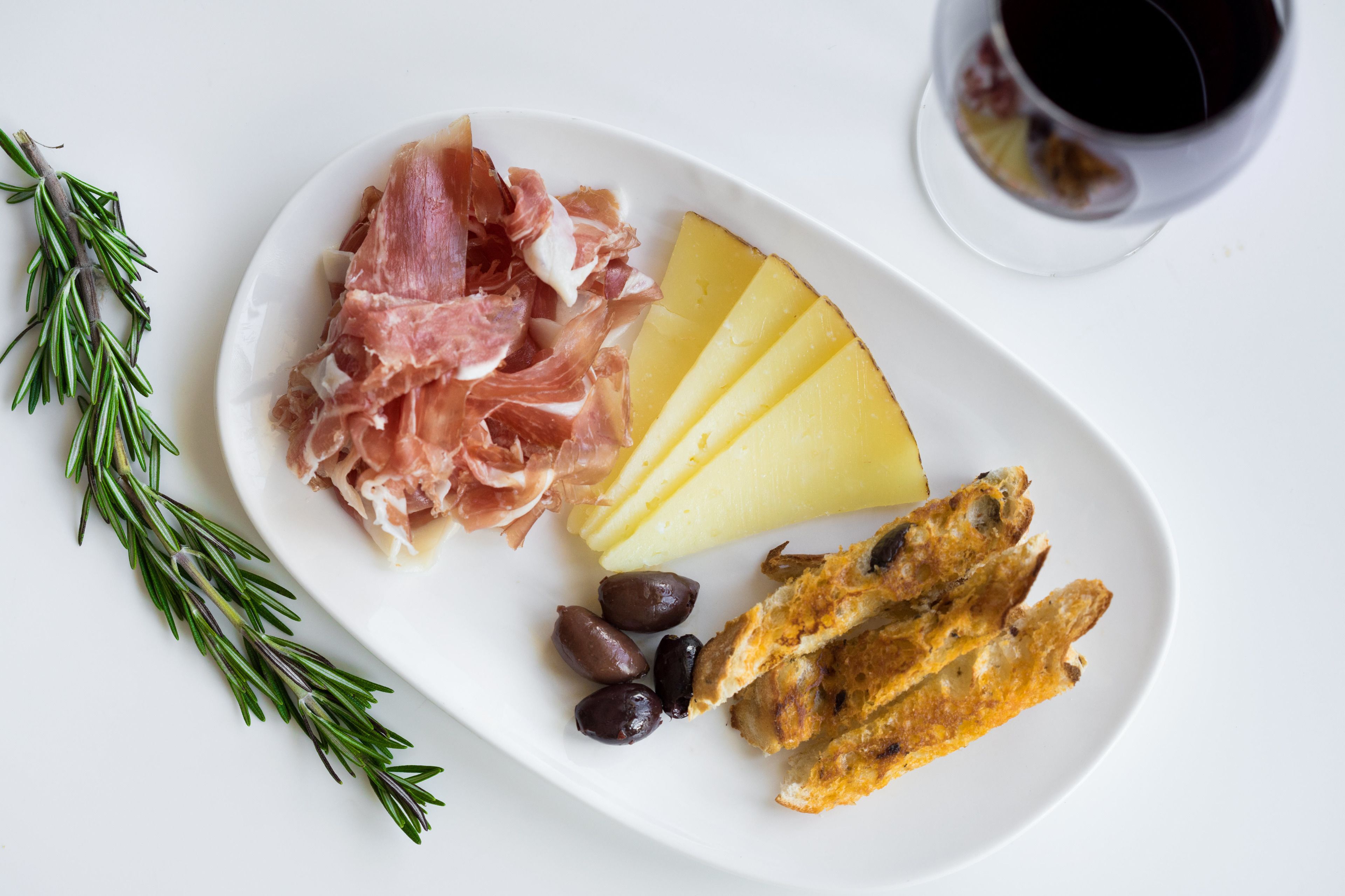 Un plato con jamón serrano, queso, aceitunas y pan sobre un fondo blanco.