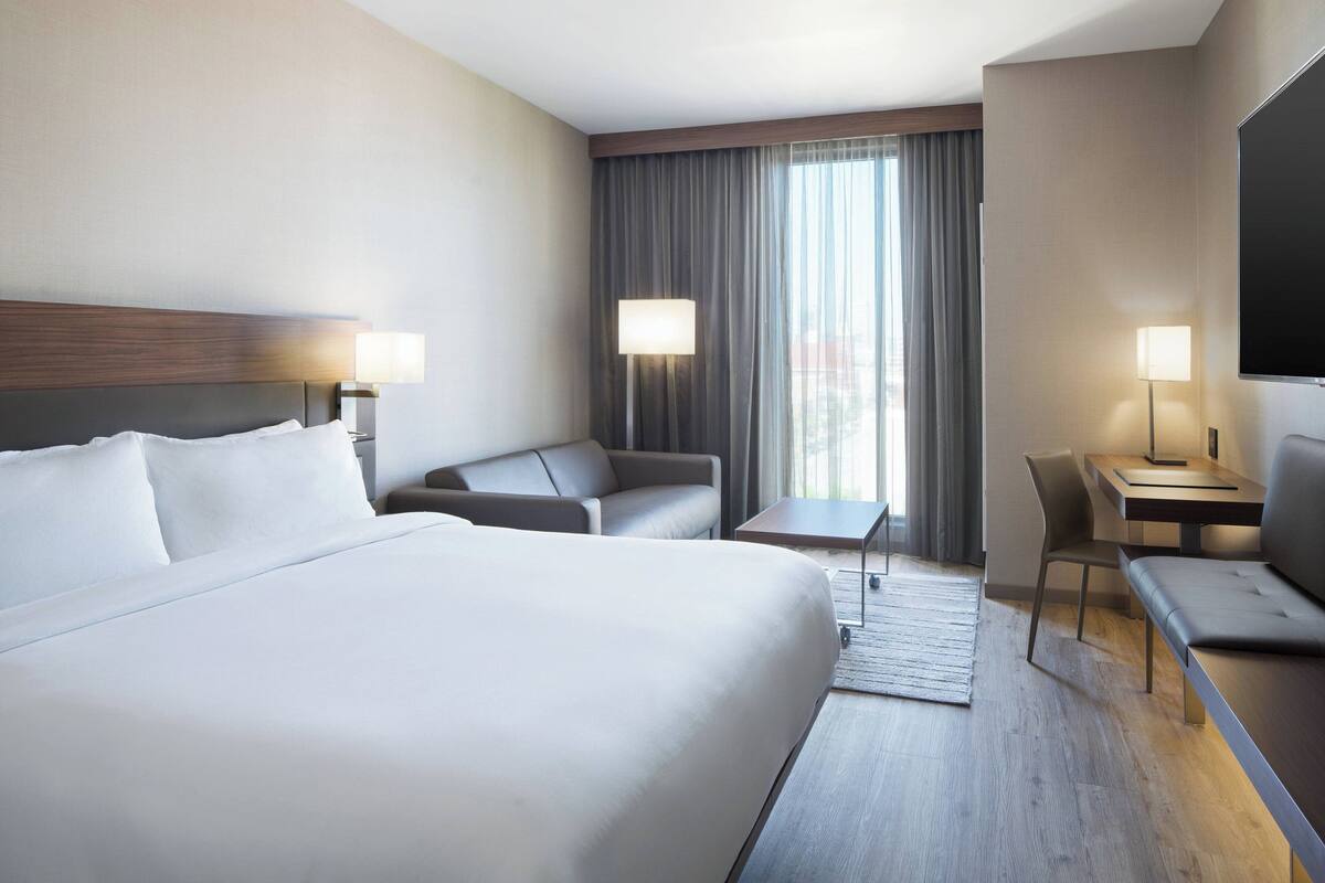 A modern hotel room with a large bed, a desk, a chair, and a sofa.
