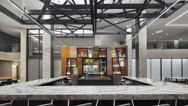 A modern bar area with a marble countertop, seating, and a central bar stocked with bottles. - AC Hotel Louisville Downtown (Louisville)