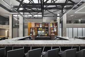 A modern bar area with a marble countertop, seating, and a central bar stocked with bottles. - AC Hotel Louisville Downtown (Louisville)