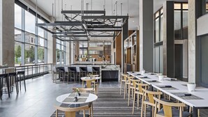 A modern restaurant with high ceilings, large windows, and a mix of round and rectangular tables. - AC Hotel Louisville Downtown (Louisville)
