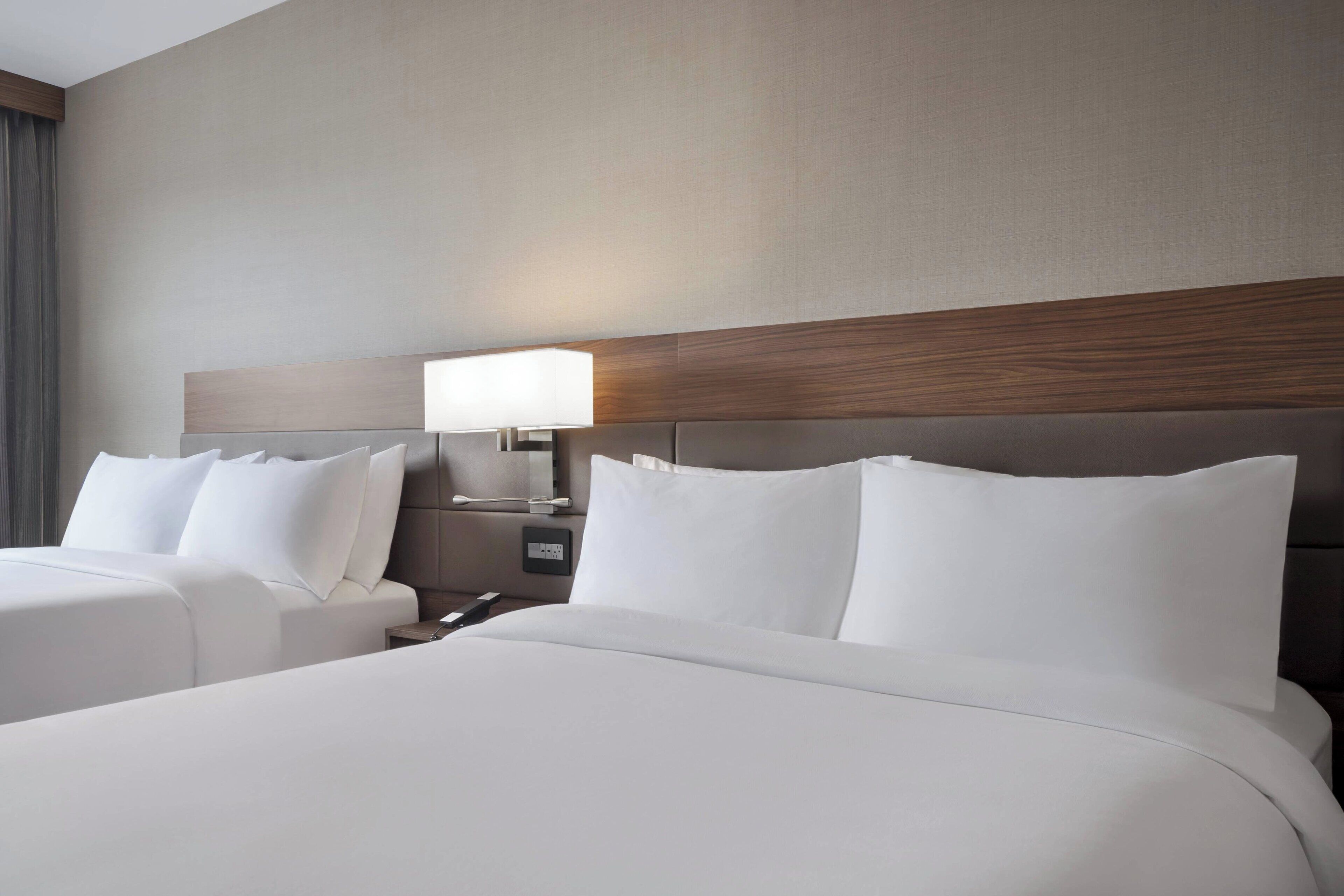 Une chambre d’hôtel avec deux lits, une table de chevet avec une lampe et une tête de lit en bois.