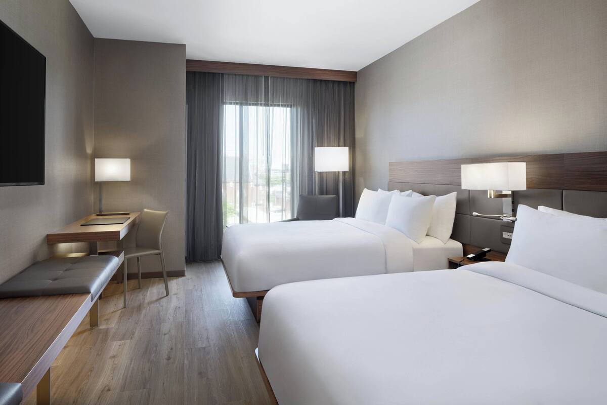 A hotel room with two beds, a desk, a chair, and a TV.
