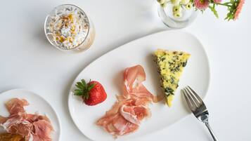 Een ontbijttafel met een bord eten, inclusief een plakje quiche, parmaham en een aardbei, plus een glas romige drank en een croissant.