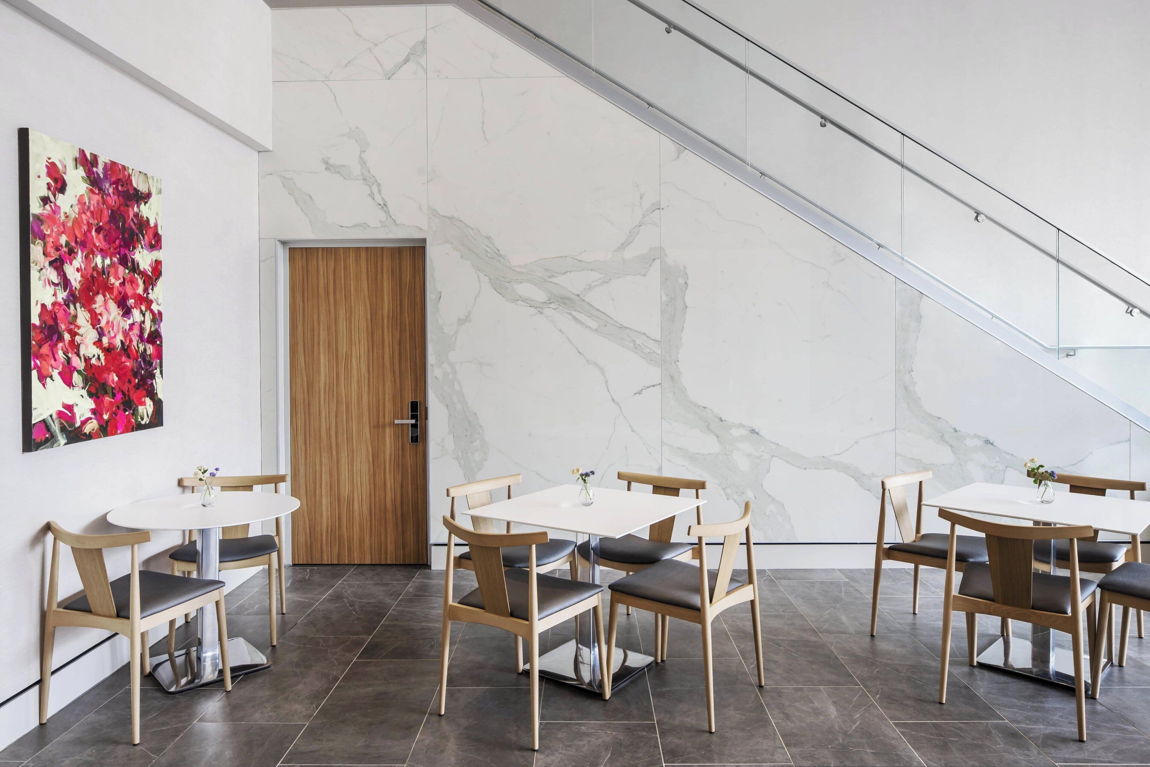 Un comedor moderno con paredes de mármol, una puerta de madera y una barandilla de cristal.