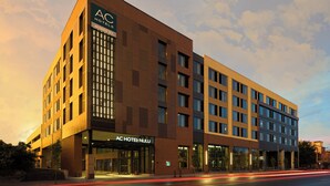 A modern hotel building with a prominent AC Hotel NULU sign, multiple floors, and a well-lit entrance. - AC Hotel Louisville Downtown (Louisville)