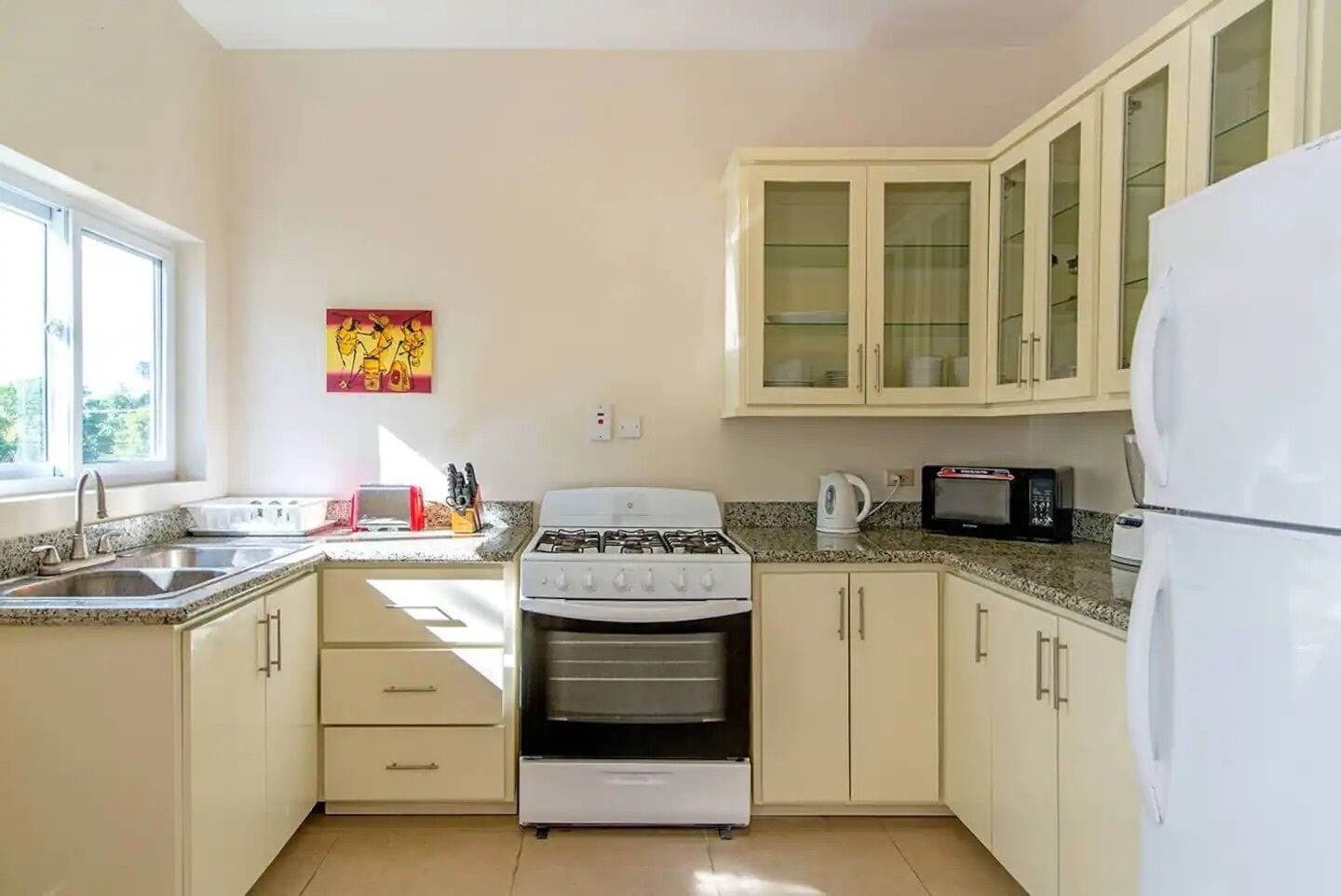 A kitchen with a gas stove, oven, microwave, and a refrigerator. There are cabinets and a window providing natural light.