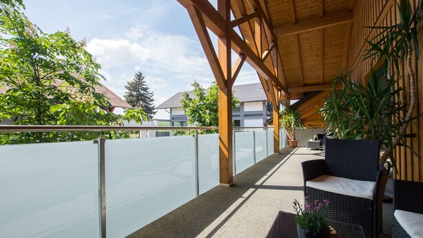 Ein Balkon im Freien mit Glasgeländer, Holzbalken und Korbmöbeln.