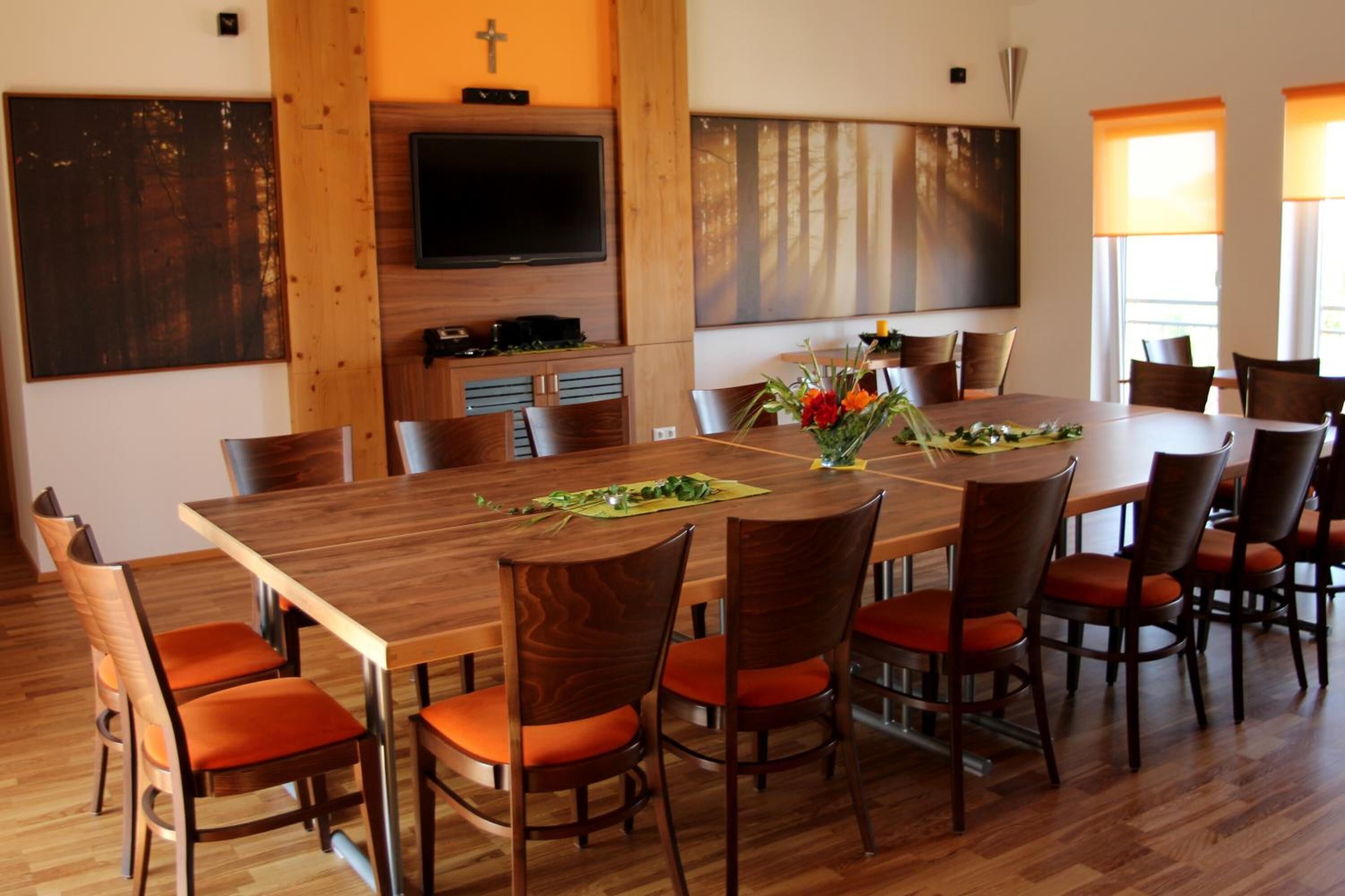 Un comedor con una mesa y sillas de madera, un televisor de pantalla plana en la pared y obras de arte en las paredes.