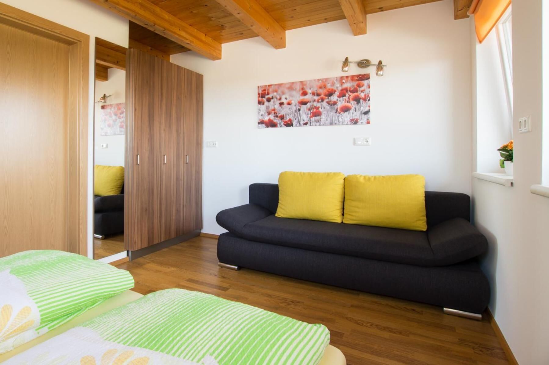 Una habitación con un sofá oscuro, dos cojines amarillos, un armario de madera y un cuadro con motivos florales en la pared.