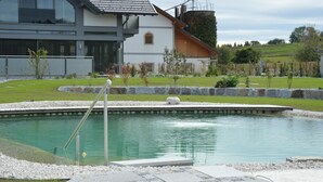 Ein modernes Haus mit Schwimmbecken, umgeben von einem gepflegten Garten und einem Holzzaun.