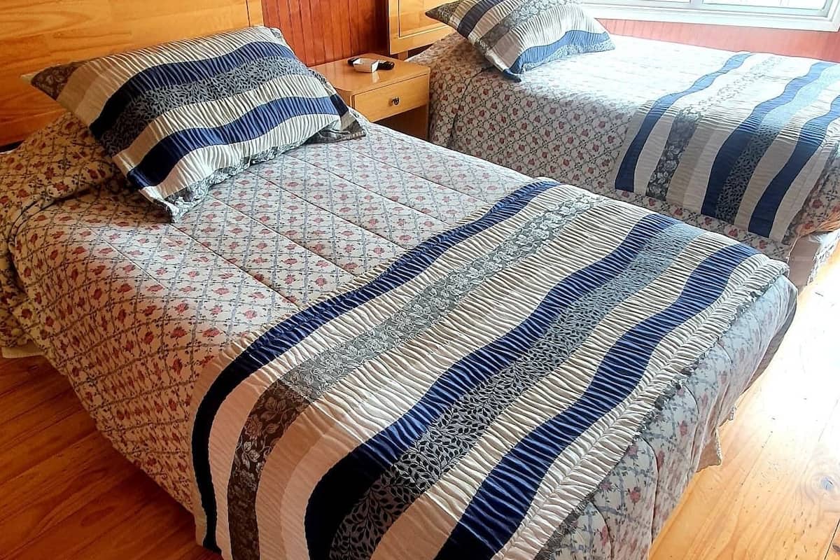 A double bed with a floral-patterned duvet and striped pillows in a room with wooden paneling and a window with blinds.