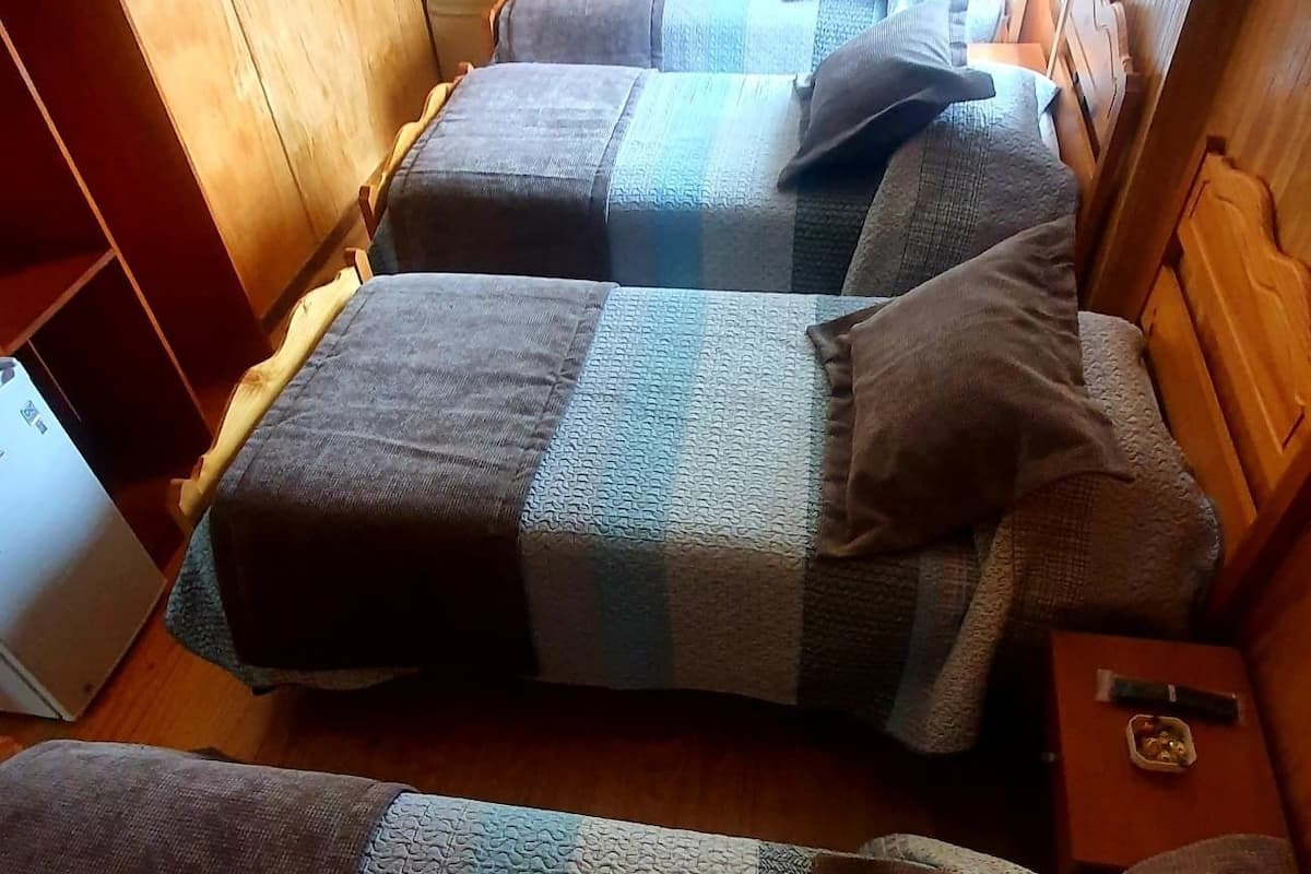 A compact cabin with two beds, each with a striped blanket and pillows. A small table with a remote control and a snack container is beside one bed.