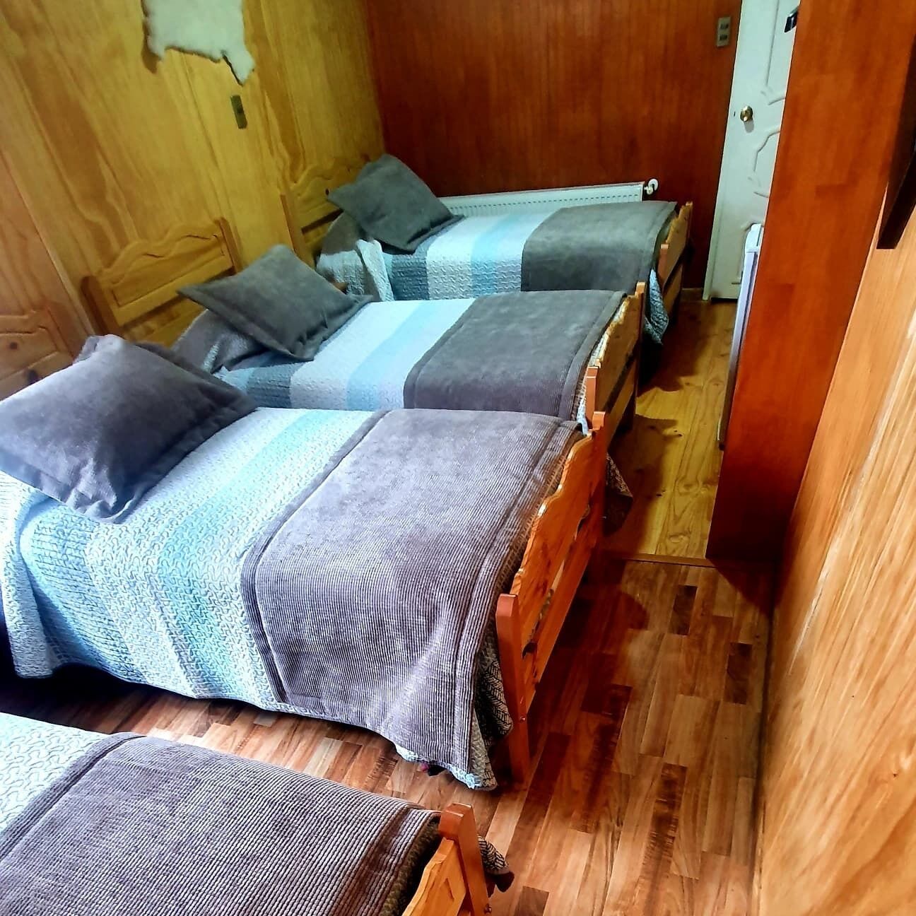 Habitación compacta con dos camas de madera, cada una con un edredón azul y gris a rayas y una almohada.