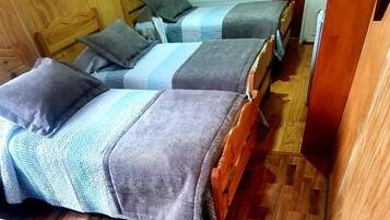 Habitación compacta con dos camas de madera, cada una con un edredón azul y gris a rayas y una almohada.