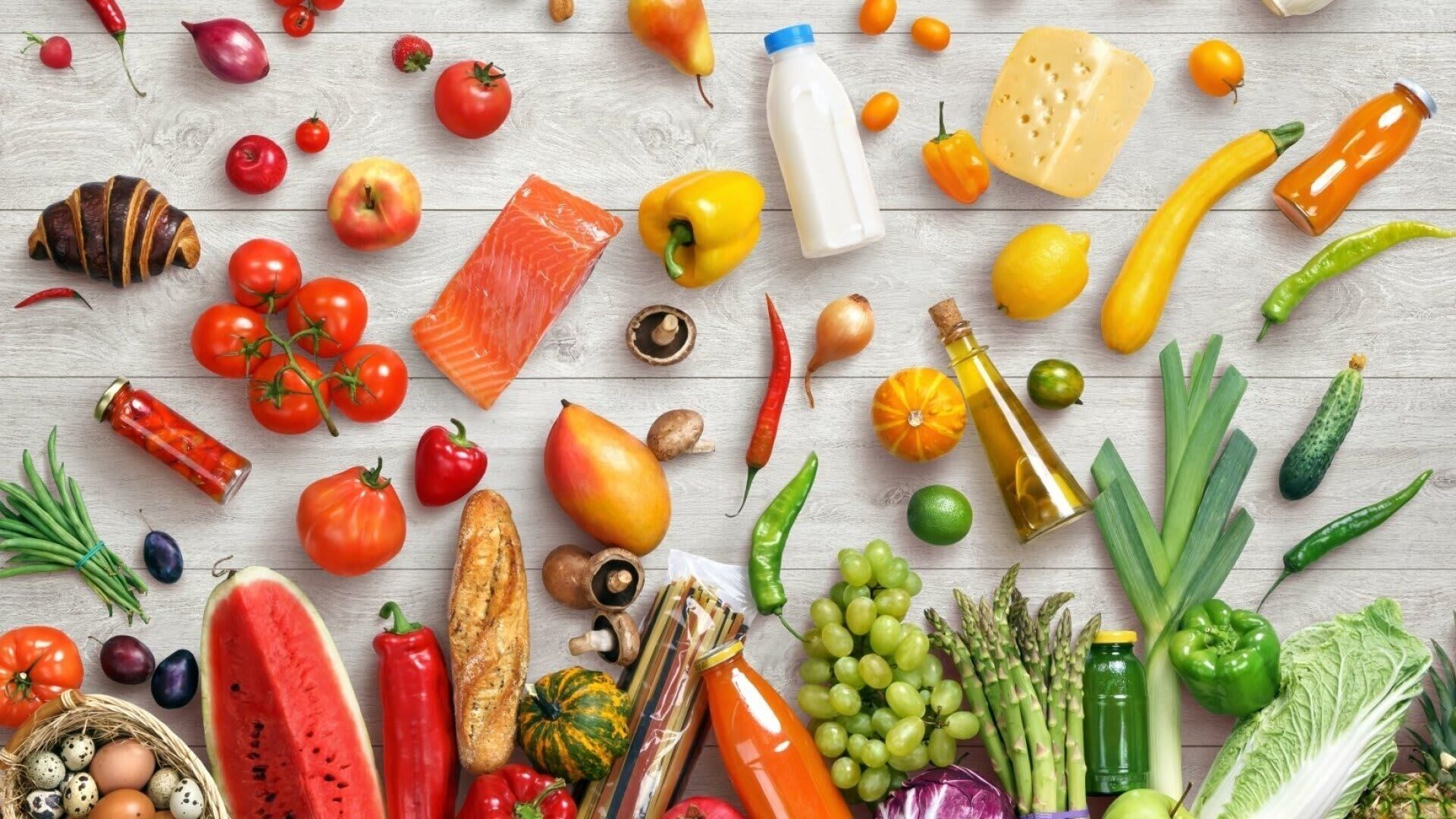 A variety of fresh fruits, vegetables, and dairy products arranged on a wooden surface.