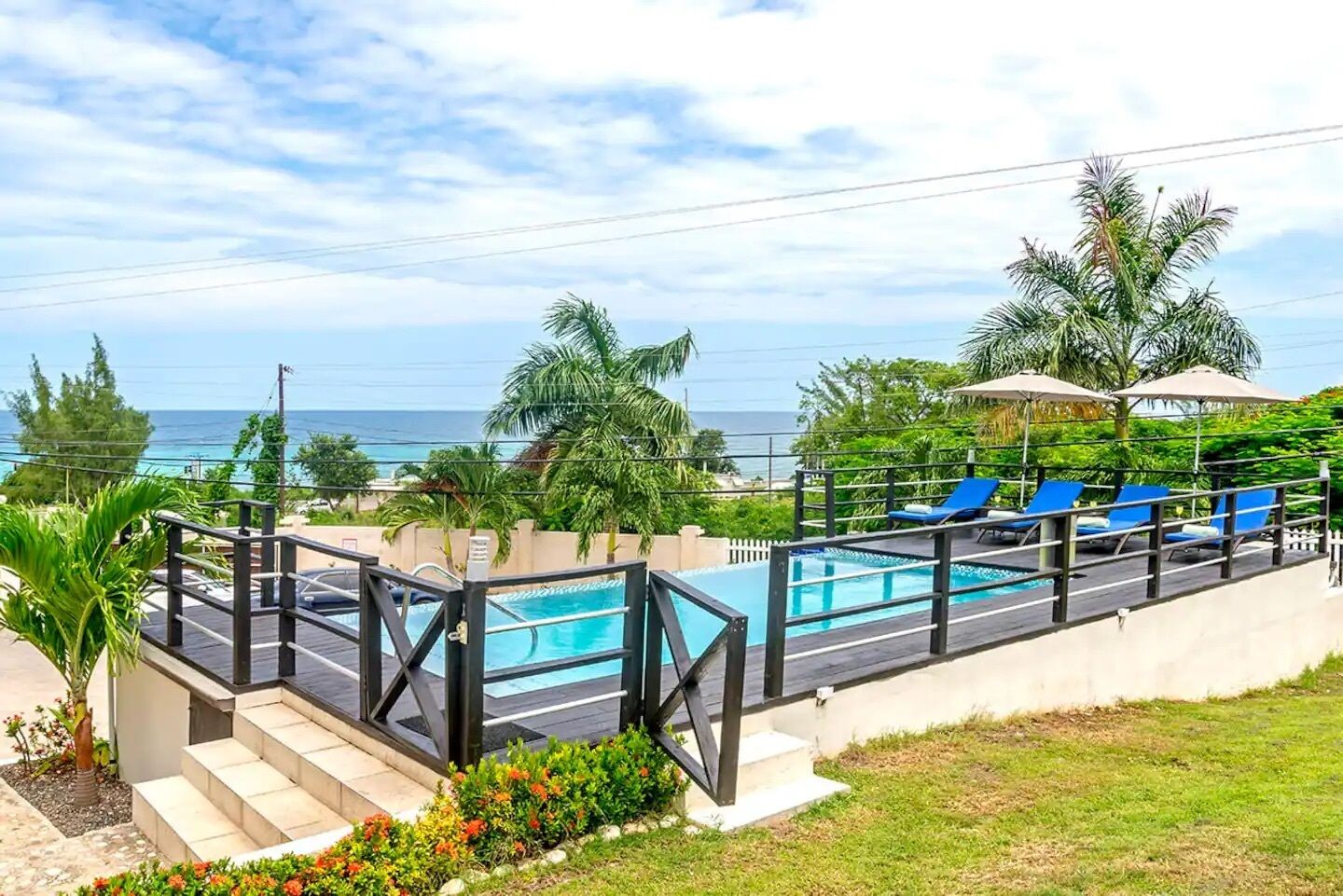 A pool area with blue lounge chairs, a wooden deck, and a view of the ocean.