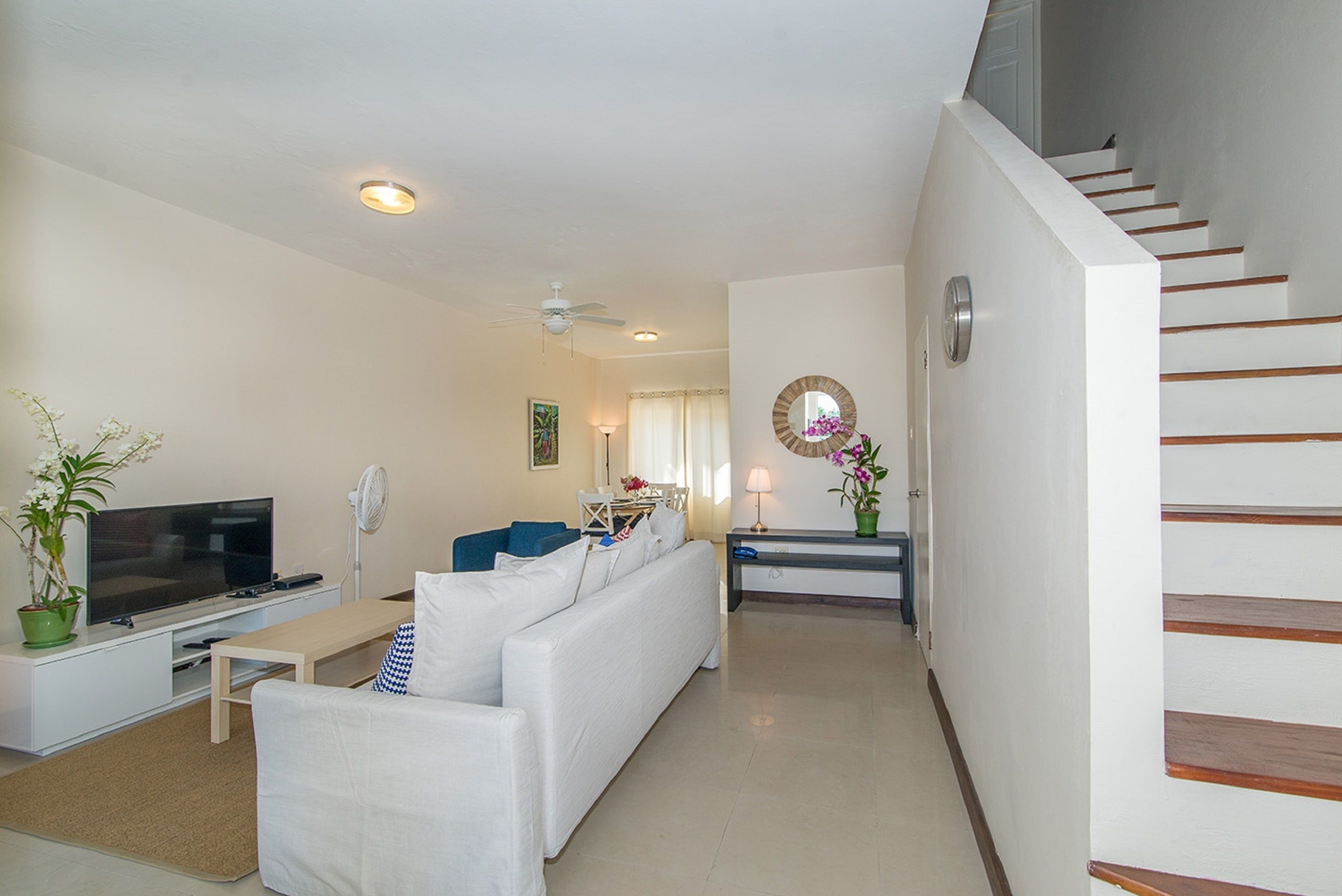 A modern living room with a white sofa, a flat-screen TV, a coffee table, and a staircase with wooden steps.