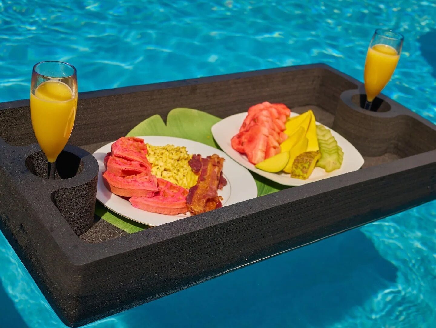 A tray with breakfast items and two glasses of orange juice by a pool.