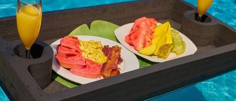 A tray with breakfast items and two glasses of orange juice by a pool.
