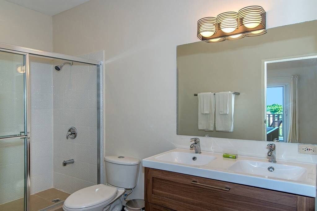 A bathroom with a glass shower enclosure, a toilet, a sink with a mirror above it, and a towel hanging on the wall.