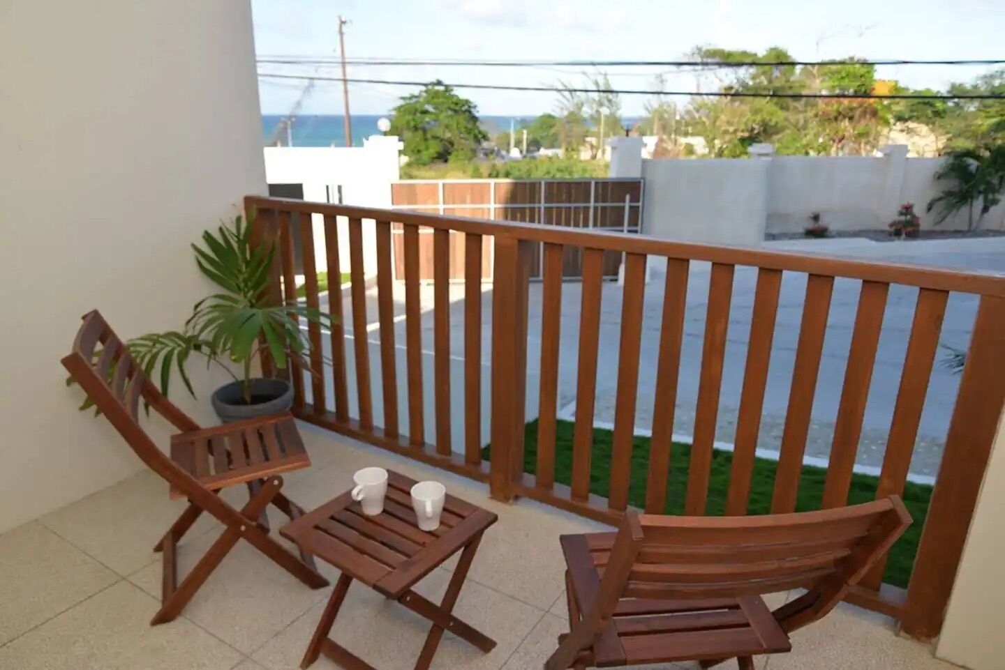 A balcony with wooden furniture, a potted plant, and a view of the street and greenery.