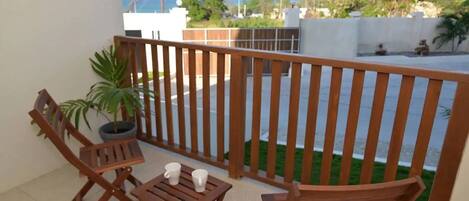A balcony with wooden furniture, a potted plant, and a view of the street and greenery.
