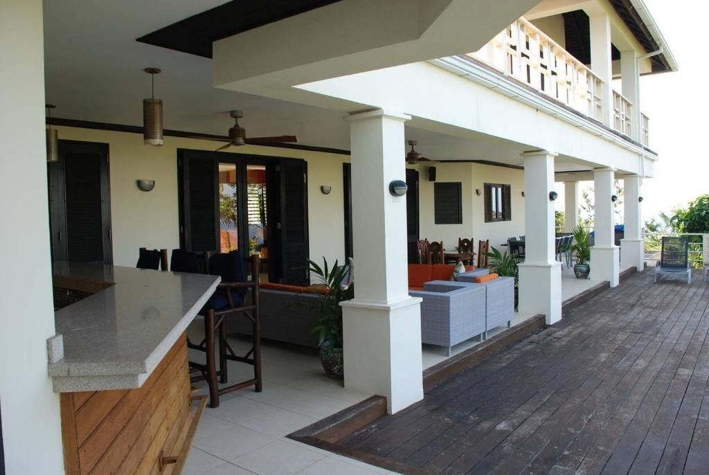 A covered outdoor area with a kitchen counter, seating, and a balcony.