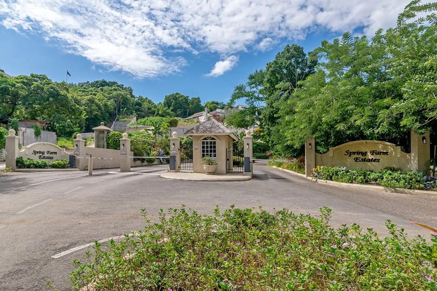 A gated entrance with a small gazebo, surrounded by lush greenery and a clear sky.