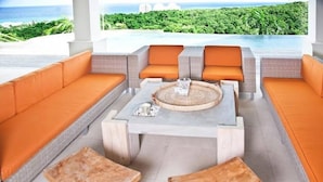 A modern outdoor seating area with orange cushions and a central table, overlooking a lush green landscape and a body of water. - Hospitality Expert SF (Montego Bay)