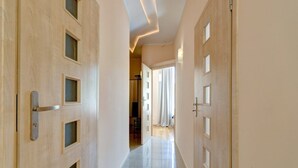 A hallway with wooden doors, a tiled floor, and a view into a room with a chair and a table. - Apartament Opera Sopot (Sopot)