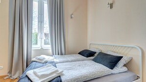 A bedroom with two beds, a window with curtains, and a lamp on the wall. - Apartament Opera Sopot (Sopot)