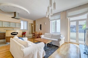 Un salon moderne avec un canapé, une table basse et un téléviseur. Il y a également un coin repas avec des chaises et une table. La pièce est dotée de grandes fenêtres et offre une vue sur les bâtiments environnants.