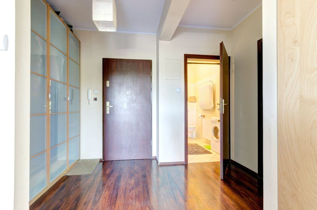 A hallway with a wooden floor, a sliding glass door, and a wooden door leading to a bathroom.