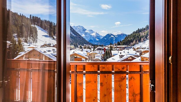 A wooden balcony with a view of a snow-covered mountain town and surrounding forest. - Hotel Cristiania (Pinzolo)