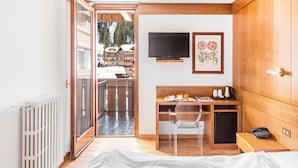 A compact room with a wooden desk, a chair, a bed, a TV, and a framed botanical print. - Hotel Cristiania (Pinzolo)