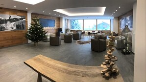 A spacious living area with a wooden bench, a Christmas tree, and a rustic wooden sculpture. - Hotel Cristiania (Pinzolo)