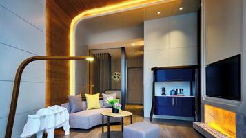 A modern living room with a sofa, ottoman, and a coffee table. There is a TV mounted on the wall and a fireplace with a stone surround.
