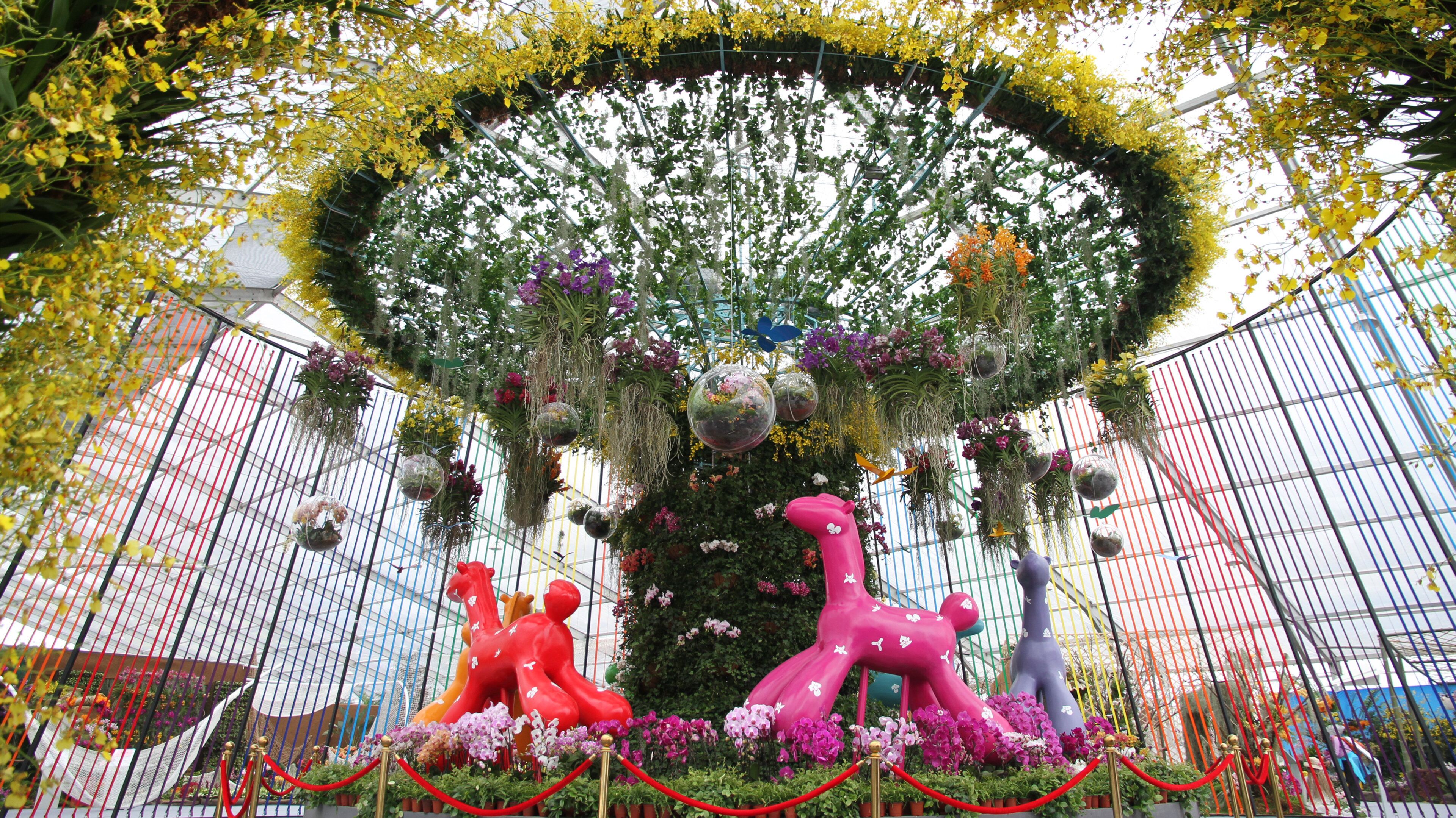 A large indoor garden with hanging plants and colorful sculptures.
