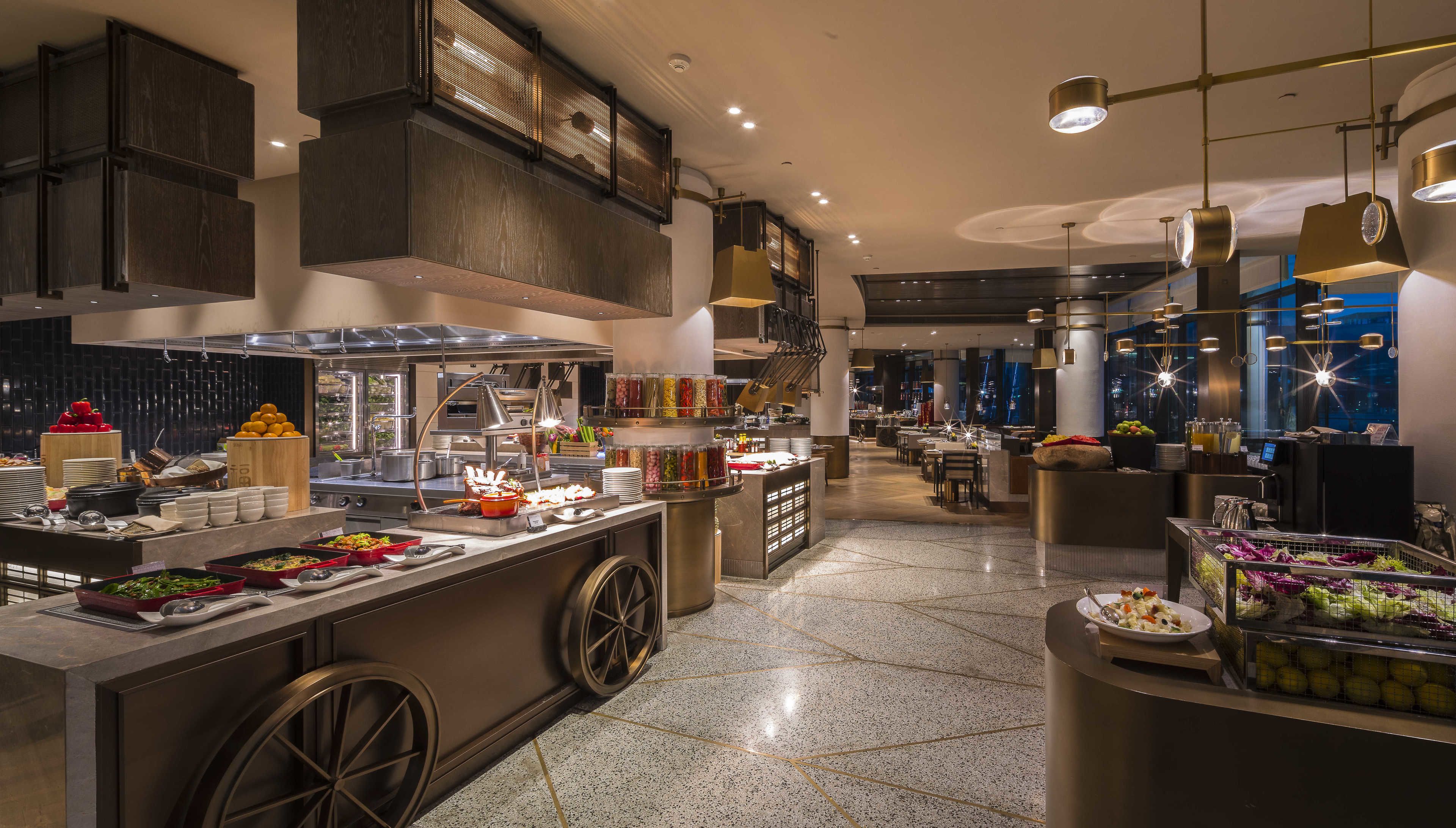 A modern hotel lobby with a buffet area, a seating area, and a view of the cityscape.