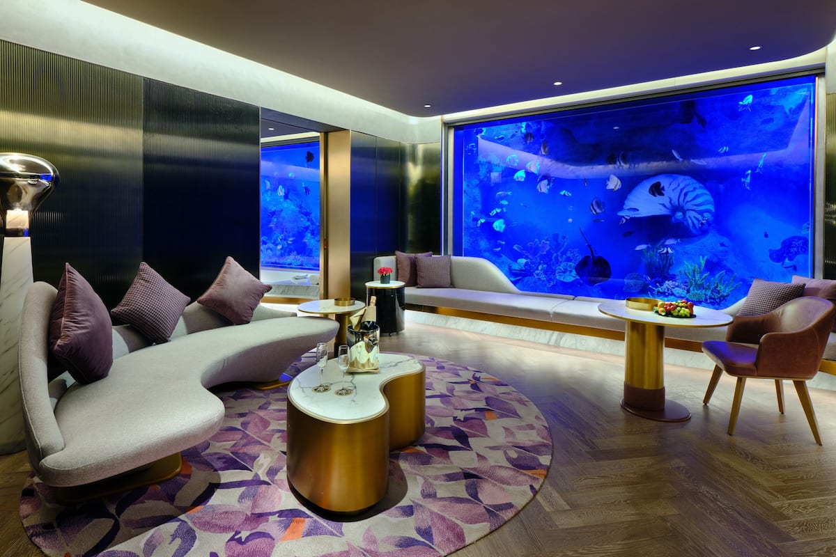 A modern lounge area with a large aquarium, comfortable seating, and a decorative rug.