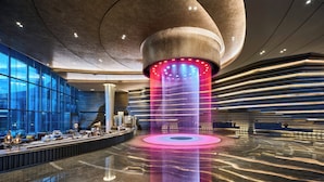 Een moderne lobby met een centraal rond lichtobject, een receptiebalie en een zithoek met uitzicht op de skyline door grote ramen.
