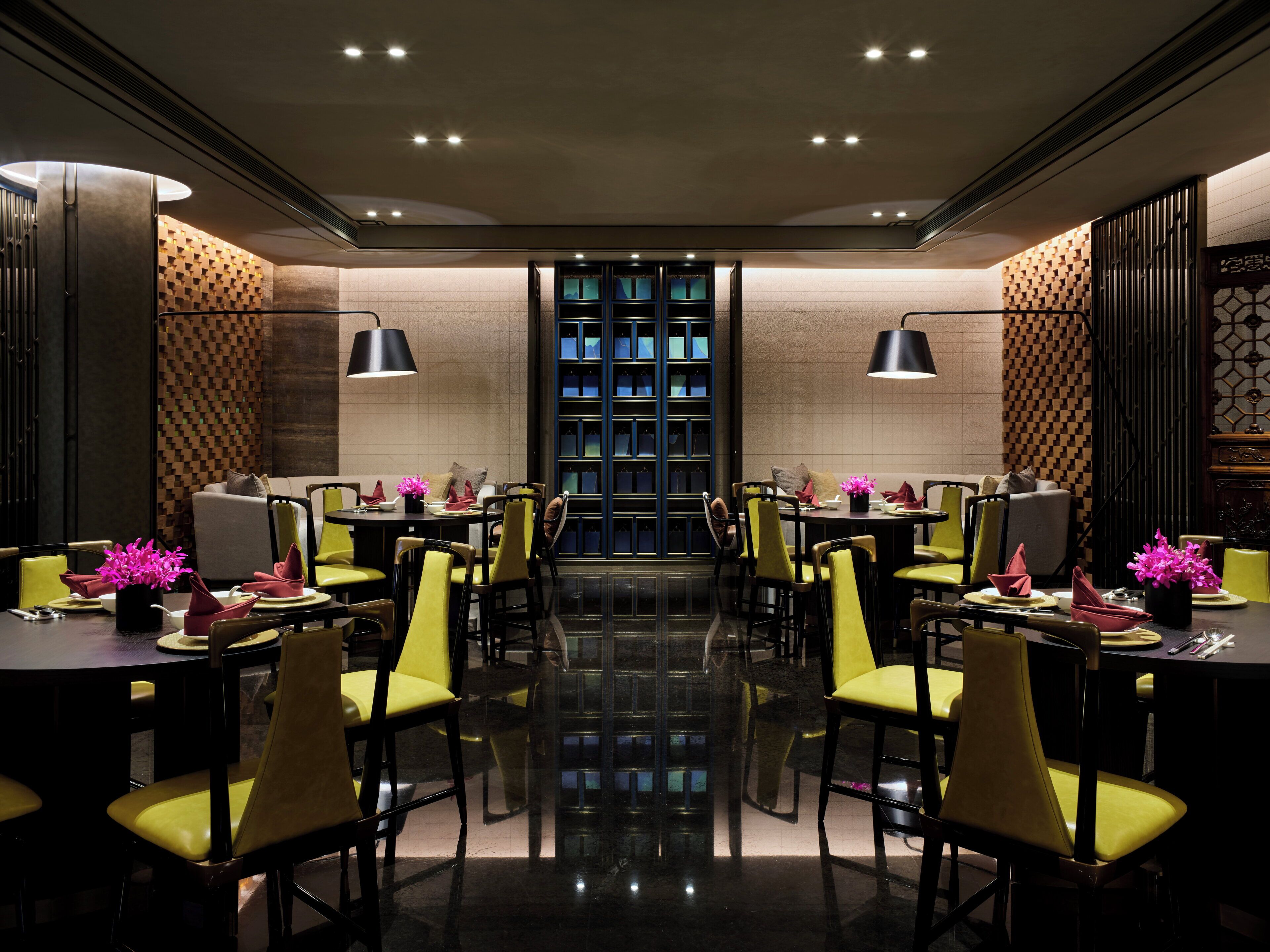 A modern dining area with multiple tables and chairs, a central bookshelf, and a reflective floor.