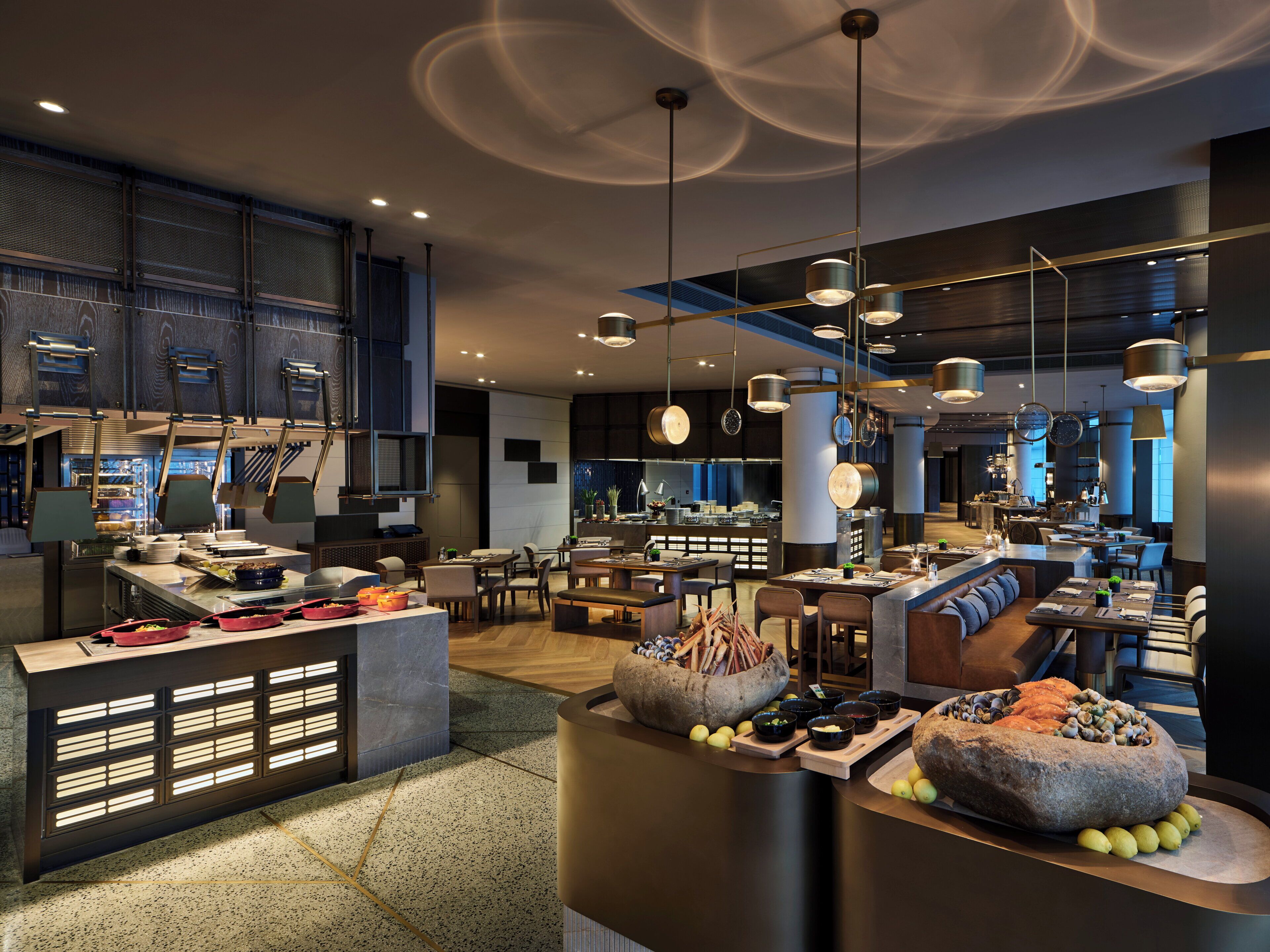 A modern restaurant with a central bar area, seating arrangements, and a kitchen in the background.